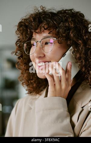 Donna d'affari biracial sorridente che parla al telefono in ufficio Foto Stock