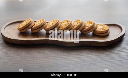 deliziosi biscotti sandwich ripieni di crema disposti su un tavolo di legno rustico. Una luce calda e soffusa evidenzia le superfici ruvide dei biscotti, la ricca crema dolce Foto Stock