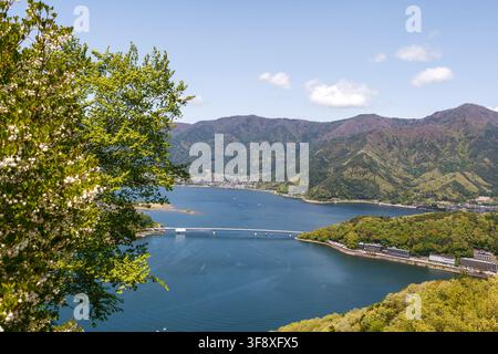 YAMANASHI, GIAPPONE - 5 LUGLIO 2025: Bella vista panoramica del lungolago di Kawaguchi con un ponte e una catena montuosa sotto un cielo azzurro in estate. Foto Stock