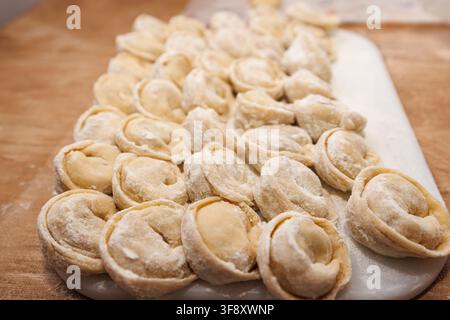 Pelmeni fatti in casa crudi coperti di farina su un tagliere bianco. Vista laterale in primo piano della preparazione tradizionale russa o dell'Est Foto Stock