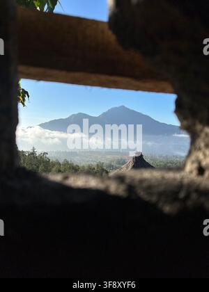Monte Agung visto dai piedi del Monte Batur, Bali, Indonesia, incorniciato da una struttura tradizionale in legno con nuvole sottostanti. Foto Stock