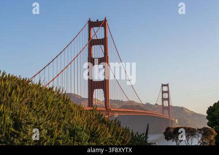 Le torri del Golden Gate Bridge si ergono dietro colline costiere verdi sotto un cielo morbido e limpido durante l'ora dorata a San Francisco, California Foto Stock