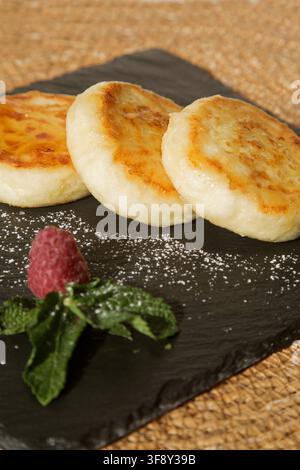 Cheesecake alla vaniglia (pancake al formaggio cottage) versati con miele su un piatto nero Foto Stock