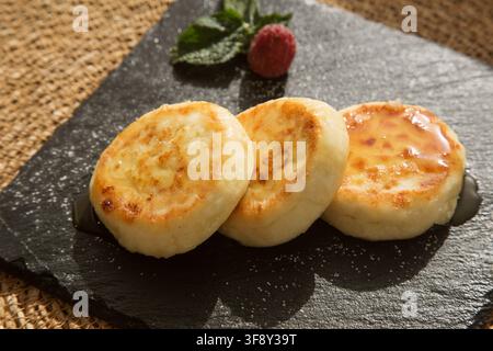 Cheesecake alla vaniglia (pancake al formaggio cottage) versati con miele su un piatto nero Foto Stock