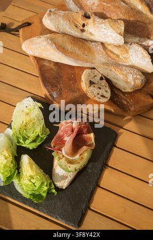 Bruschetta con prosciutto (pancetta) e avocado su un piatto nero. L'opzione per una colazione o uno spuntino bello e sano Foto Stock