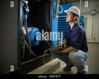 Tecnico che utilizza software di test su un computer portatile per monitorare le vibrazioni nelle attrezzature di produzione, New York, USA Foto Stock