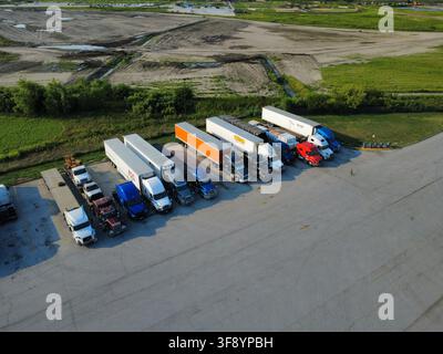 Vista aerea con drone di semi-treni e rimorchi parcheggiati accanto a un cantiere edile di scavi attivo nel Midwest americano. Foto Stock