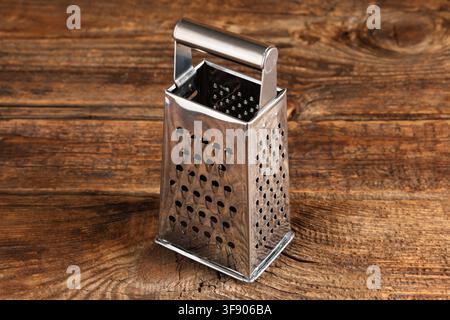Grattugia in acciaio inossidabile con quattro superfici di grattatura e un manico in metallo su un tavolo di legno rustico, la grattugia presenta più superfici di grattatura e un Foto Stock