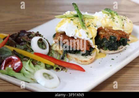 Uova Benedict con pulled pork e spinaci appassiti su muffin inglesi tostati, ricoperti di salsa olandese e asparagi, serviti con una salsa fresca a lato Foto Stock