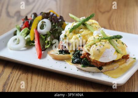Uova Benedict con pulled pork e spinaci appassiti su muffin inglesi tostati, ricoperti di salsa olandese e asparagi, serviti con una salsa fresca a lato Foto Stock