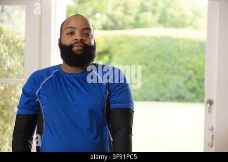 Uomo afroamericano in piedi davanti a una porta aperta in casa con una camicia blu, la maniglia della porta è visibile Foto Stock