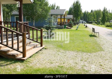 Scalini in legno della terrazza nel villaggio di cabine per le vacanze. Concetto di stile di vita lento ecoturistico all'aperto accogliente. Giardino del parco estivo tranquillo per la famiglia Foto Stock