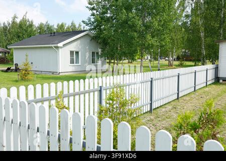 Recinzione bianca attorno a un moderno cottage di vacanza in campagna. Concetto di stile di vita all'aperto ecoturistico e lento accogliente. Famiglia in un giardino di parco tranquillo estivo Foto Stock