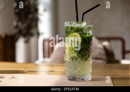 Un mojito ghiacciato servito in un bicchiere highball strutturato con cannucce nere su un tavolo, catturando l'essenza fresca e sapiente di un classico vacat Foto Stock