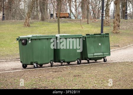Grandi contenitori di spazzatura in plastica sono allineati lungo un sentiero in un giardino boscoso, rappresentando una manutenzione ambientale municipale efficiente e organo Foto Stock
