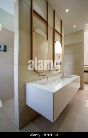 Vista prospettica di un interno di bagno moderno ed elegante che mostra un doppio lavandino galleggiante bianco con rubinetti cromo eleganti. L'area del mobile lavabo. Foto Stock