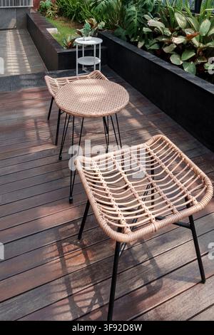 Set moderno di mobili per terrazzo con sedie in vimini sintetico intrecciato leggero con gambe in metallo nero e un tavolo rotondo abbinato. Foto Stock