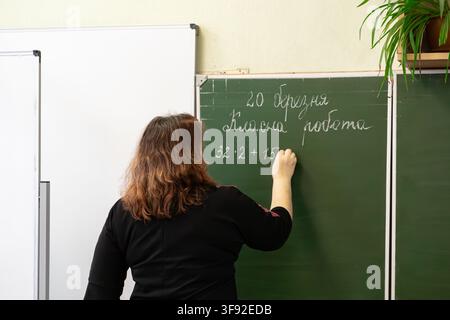 Un educatore scrive problemi matematici su una lavagna in un'aula primaria luminosa, evidenziando l'eccellenza didattica e la ricerca dell'eccellenza Foto Stock