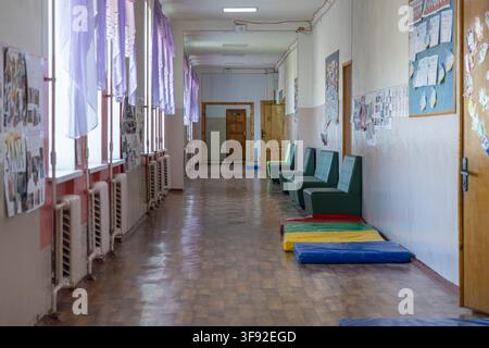 Un tranquillo corridoio di una scuola elementare include piccole sedie a sdraio e tappetini da gioco vivaci per i bambini, offrendo uno spazio accogliente all'interno dell'edificio per Foto Stock