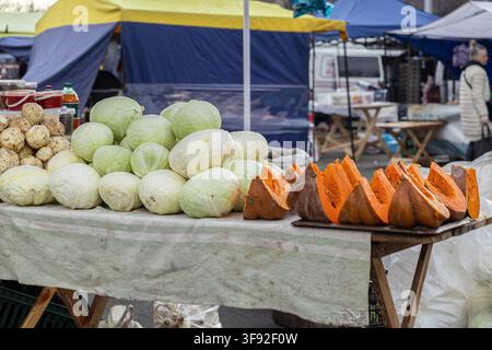 Mucchi di teste di cavolo verde e spicchi di zucca luminosi disposti su uno stand in un mercato contadino, che mostrano prodotti stagionali crudi e naturali e salutari Foto Stock