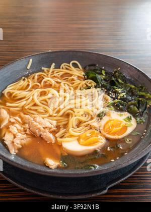 La zuppa gourmet di ramen con brodo saporito, noodles di grano elastici e semi di sesamo serviti in una ciotola di ceramica scura, evocando il calore e il comfort di un t Foto Stock