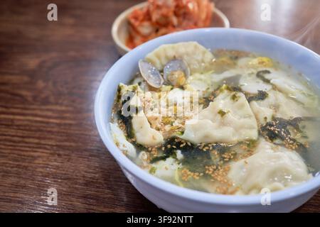 Zuppa tradizionale coreana di dumpling tteokmanduguk con torte di riso affettate, strisce di uovo e vongole servite insieme al kimchi di cavolo napa in un ristorante locale Foto Stock