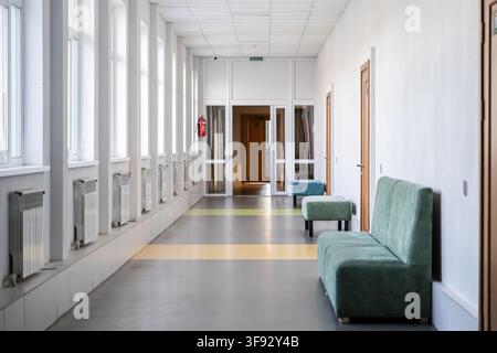 Un corridoio vuoto in una clinica moderna mette in mostra comodi divani di velluto e luce naturale del giorno proveniente dalle finestre laterali per trasmettere un ambiente tranquillo per il paziente Foto Stock