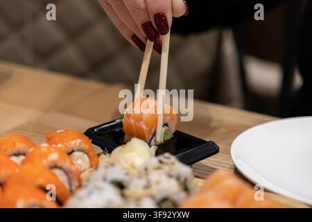 Un primo piano di una persona che usa bacchette di legno per intingere del nigiri di salmone fresco in un piccolo contenitore di salsa di soia, catturando un momento culinario raffinato in un M Foto Stock