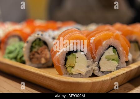 Appetitosi sushi maki Philadelphia disposti ordinatamente su un vassoio di legno, evidenziando la texture vivace del pesce e i ripieni cremosi per una culi di alto livello Foto Stock