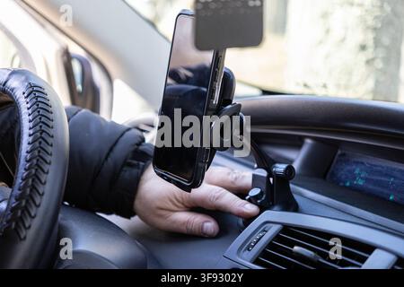 Una mano si protende per fissare un telefono cellulare su un supporto per cruscotto all'interno di un'automobile, mostrando soluzioni di navigazione intelligenti per i conducenti che apprezzano la sicurezza Foto Stock