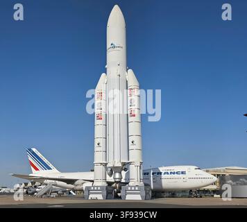 Modello a grandezza naturale del veicolo di lancio spaziale Ariane 5 in piedi all'aperto accanto a un aereo di linea Air France Boeing 747 sotto un cielo blu terso. Foto Stock