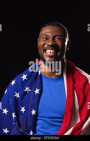 Uomo afroamericano di mezza età che sorride mentre indossa una bandiera americana e una camicia blu in studio Foto Stock