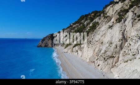 Splendida veduta aerea di una spiaggia isolata con acque turchesi che incontrano drammatiche scogliere di calcare bianco ricoperte di vegetazione verde. Foto Stock