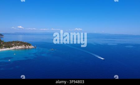 Splendida veduta aerea di una costa mediterranea con acque basse turchesi che passano al mare blu profondo, con una barca a motore che lascia una scia bianca Foto Stock