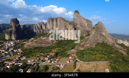 Stupenda veduta aerea degli enormi pilastri di roccia di arenaria di Meteora che si ergono sopra un villaggio tradizionale greco, incorniciati da un cielo azzurro e nuvole sparse Foto Stock
