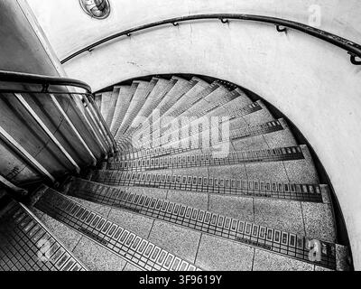 Vista in bianco e nero dall'alto di una stretta scala a chiocciola curva e ringhiere metalliche in una stazione della metropolitana del centro di Londra Foto Stock