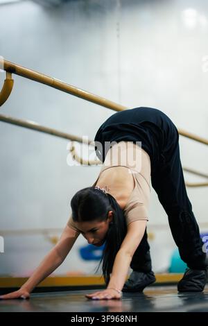 Ballerina si allunga sul pavimento prima della sessione di pratica in uno studio con la sbarra sullo sfondo Foto Stock