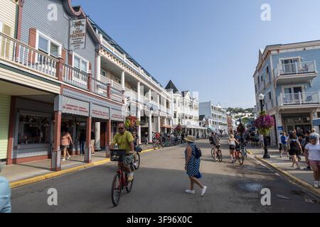 Mackinac Island, Michigan, Stati Uniti - 15 agosto 2025: Vista della vivace Main Street con facciate di negozi storici, ciclisti, pedoni e hang Foto Stock