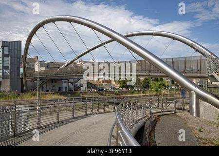 Vista laterale a bassa altezza che mostra la rampa di accesso curva e i doppi archi in acciaio inossidabile del ponte Celtic Gateway a Holyhead, nel nord del Galles, Regno Unito. Foto Stock