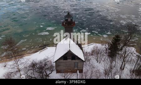 Vista aerea del faro di Grand Island circondato da terreno coperto di neve e acqua ghiacciata a Munising, Michigan, Stati Uniti. Foto Stock