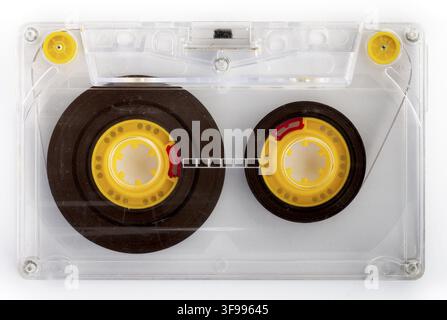 Cassetta audio trasparente con bobine di nastro gialle e guide del nastro su sfondo nero Foto Stock