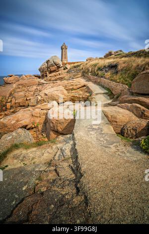 Il faro di Mean Ruz con le rocce rosse della Côte de Granit Rose in primo piano, Bretagna, Francia Foto Stock