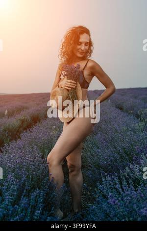 Campo di lavanda di una giovane donna in bikini e cappello che posa in un bellissimo campo di lavanda durante il tramonto nella Provenza, Francia Foto Stock