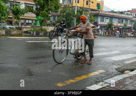 Pokhara, Provincia di Gandaki, Nepal – 2 luglio 2026: Vista di un uomo che spinge una bicicletta carica di cartone su una strada bagnata a Pokhara. Foto Stock