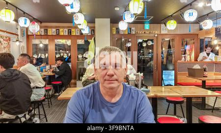 Ritratto di un cliente europeo di mezza età a un tavolo di legno in una taverna accogliente con lanterne colorate e persone che cenano sullo sfondo Foto Stock