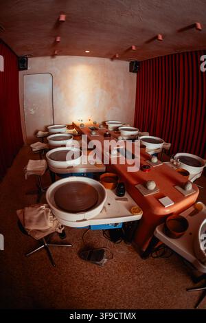 Studio di ceramica vuoto preparato per un masterclass pratico, con più ruote da vasaio, palline di argilla, strumenti, ciotole d’acqua, spugne, asciugamani e sgabelli, s Foto Stock