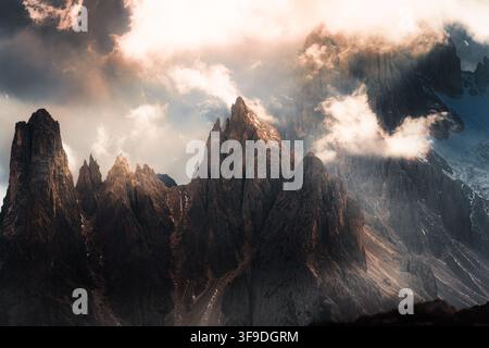 Paesaggio alpino drammatico di una cima rocciosa frastagliata che si erge attraverso le nuvole di tempesta con una luce dorata calda e nebbia nelle Tre Cime di Lavaredo, Dolomiti Foto Stock