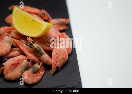 Gamberetti congelati sono disposti casualmente su una tavola di pietra nera con bordo irregolare, una fetta di limone Foto Stock