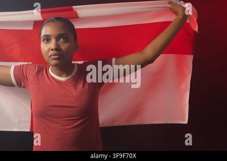 Donna afroamericana che tiene una bandiera rossa e bianca dietro le spalle in studio indossando una maglietta Ringer Foto Stock