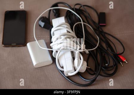 Collezione di cavi di ricarica elettronici, adattatore di alimentazione e smartphone su una superficie ruvida, che mostra varie opzioni di connettività Foto Stock
